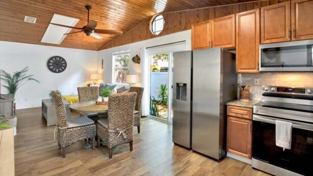 Une cuisine moderne avec des meubles en bois, des appareils électroménagers en acier inoxydable et un coin repas doté de chaises en osier.