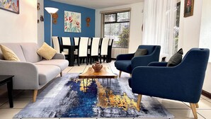 Een woonkamer met een grijze bank, blauwe fauteuils, een houten salontafel en een kleurrijk vloerkleed.