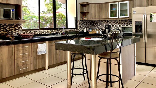 Een moderne keuken met een groot eiland, roestvrijstalen apparatuur en uitzicht op groen.