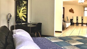 Een kamer met een bed, een bureau en een stoel. Er is een zithoek met een tafel en stoelen.