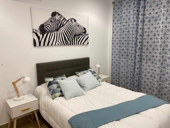 Ein Schlafzimmer mit einem Bett, Nachttischen, einer Lampe, einem gemusterten Vorhang und einem Wandbild mit Zebra-Motiv.