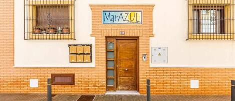 Een gebouw met een bord met de tekst 'MarAZUL' boven de ingang, een houten deur en een raam met metalen tralies.