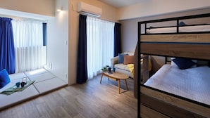 Una habitación de hotel con una cama litera, un sofá, una mesita y una ventana con cortinas.