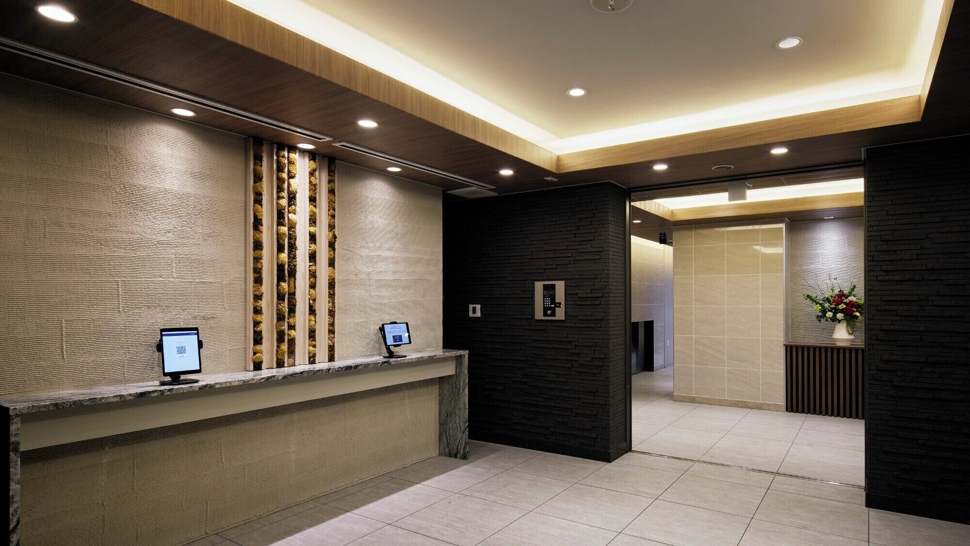 A modern reception area with a textured wall, a reception desk, and a digital display.