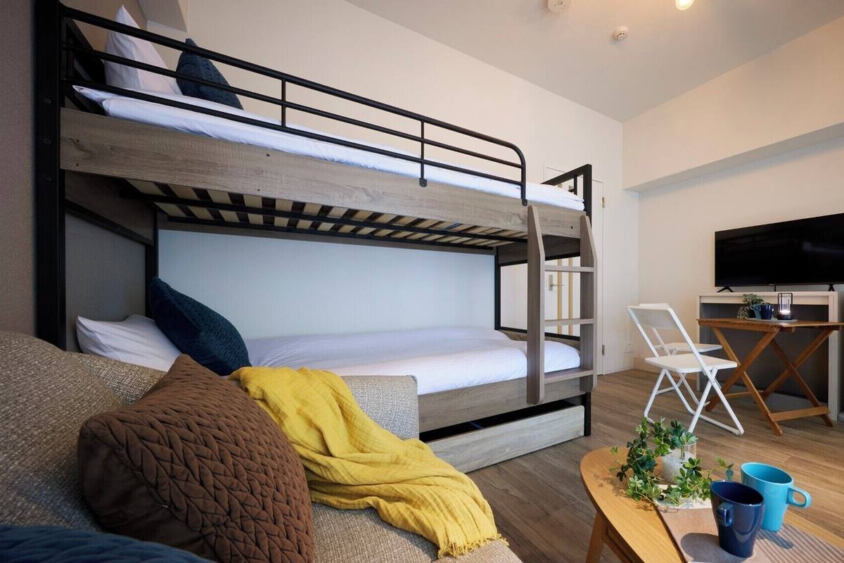 Une chambre avec un lit superposé, une télévision, un bureau et un canapé.