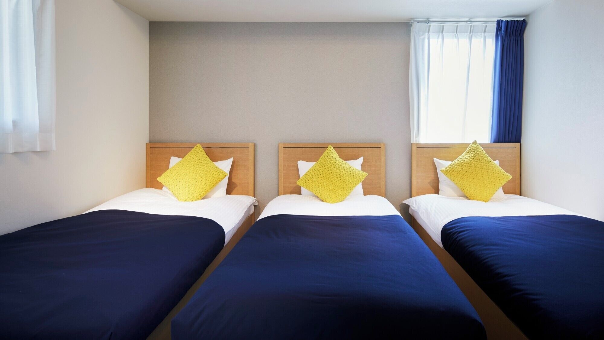 Een hotelkamer met drie eenpersoonsbedden, elk voorzien van een houten hoofdbord en een geel kussen.