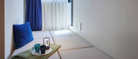 A cozy seating area with a cushioned bench, a blue pillow, a tray with two mugs, and a lantern.