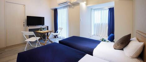 A hotel room with two beds, a desk with a chair, a TV, and a window with curtains.