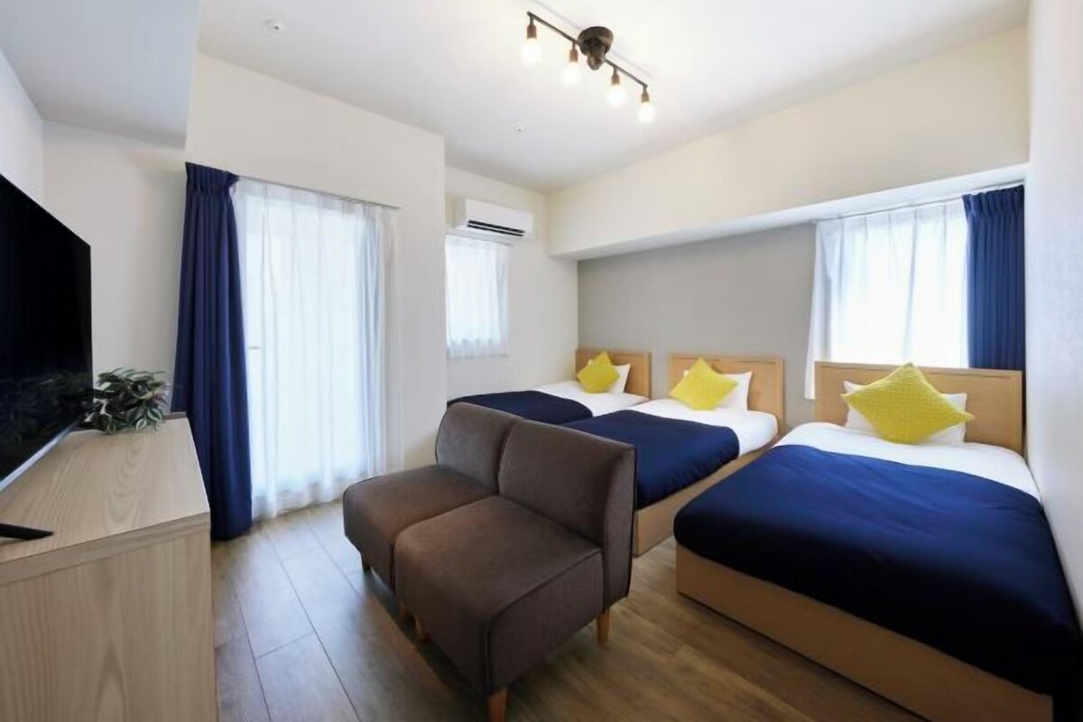 A hotel room with two beds, a sofa, a TV, and a window with curtains.