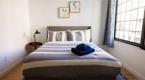 Relax in a cozy retreat with a neatly made bed, a bedside table, and a window offering a view of the outside.