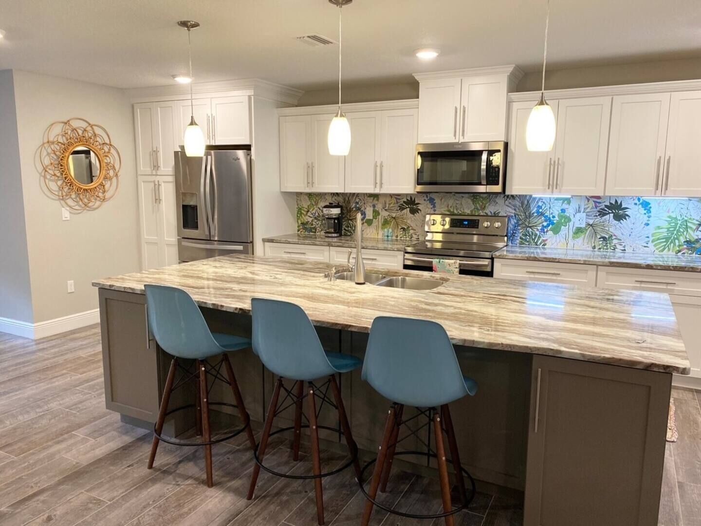 Una cocina moderna con armarios blancos, electrodomésticos de acero inoxidable y una isla de mármol con taburetes de bar.