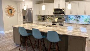 A modern kitchen with white cabinets, stainless steel appliances, and a marble island with bar stools. - Welcome to Let's Flamingle, located directly on Blue Cove just off of Rainbow River (Dunnellon)