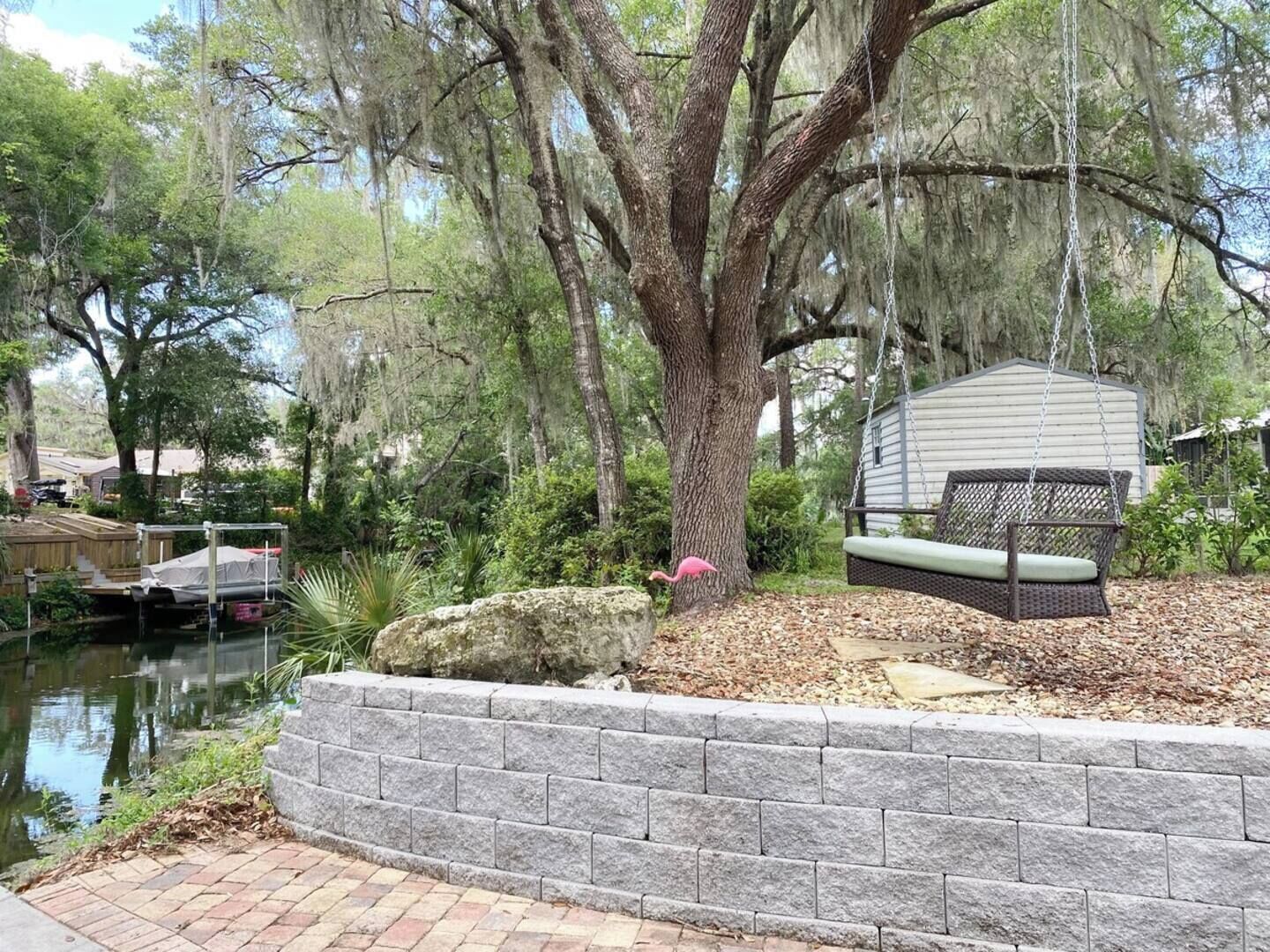 A backyard with a pond, a stone wall, a swing, and a covered seating area.
