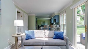 A living room with a grey sofa, a small round table with a lamp, and a remote control on the floor.