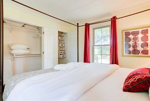 Ein ordentlich eingerichtetes Schlafzimmer mit einem Bett, einem Kleiderschrank und einem Fenster mit roten Vorhängen.