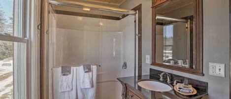 A bathroom with a glass shower enclosure, a wooden vanity with a sink, and a large mirror.