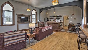 A spacious living area with a fireplace, a sofa, a dining table, and a kitchen in the background. - Renovated Historic Church Along Namekagon River! (Hayward)