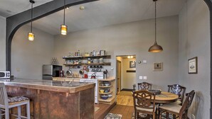 A kitchen with a central island, wooden chairs, a dining table, and hanging pendant lights. - Renovated Historic Church Along Namekagon River! (Hayward)