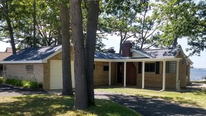A single-story house with a covered porch, a brick chimney, and a view of a body of water.