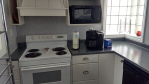 A compact kitchen with white cabinets, a white stove, a black microwave, a coffee maker, and a window with a view of the outside.