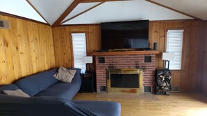 A cozy living room with a blue sofa, a brick fireplace, and wooden walls.