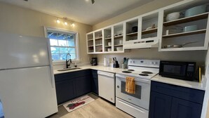 A compact kitchen with white appliances, a window, and a Christmas mat.