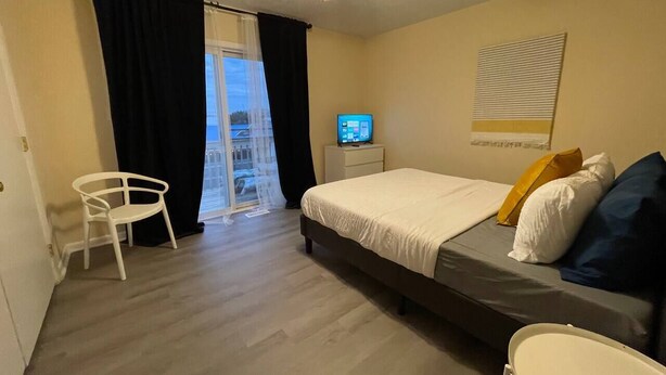 A bedroom with a bed, a desk, a chair, and a window with curtains.