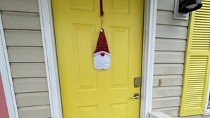 A yellow front door with a Santa hat decoration, a white porch railing, and a doormat with a leaf pattern.