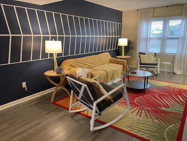 A modern living room with a sofa, a rocking chair, a coffee table, and a side table with lamps.