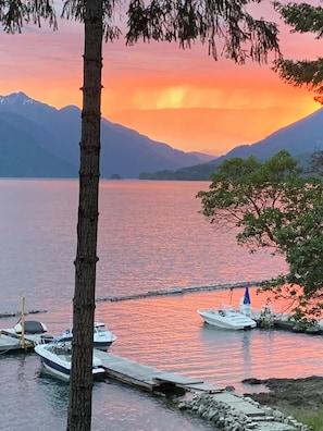 A serene lakeside scene with boats docked at a pier, surrounded by mountains and trees. - Pet-Friendly Sproat Lake Suite | Private Dock, Paddleboard/Kayaks, Firepit (Port Alberni)