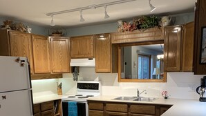 A kitchen with wooden cabinets, a white refrigerator, a stove, and a sink. - Pet-Friendly Sproat Lake Suite | Private Dock, Paddleboard/Kayaks, Firepit (Port Alberni)