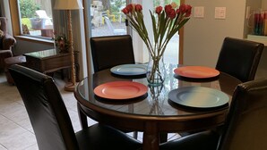 A dining area with a round table set for four, surrounded by dark leather chairs. A vase with red flowers is placed on the table, and a chandelier hangs above. - Pet-Friendly Sproat Lake Suite | Private Dock, Paddleboard/Kayaks, Firepit (Port Alberni)