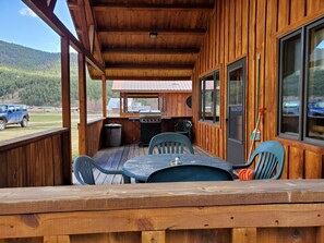 A wooden deck with a table and chairs, a grill, and a view of a forested area.