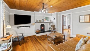 Una sala de estar con chimenea, piso de madera, un sofá, una mesa de centro y un televisor montado en la pared.