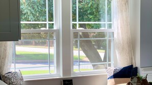 A kitchen with a large window, a hanging light fixture, and a notebook on the windowsill.