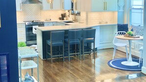 A modern kitchen with white cabinets, a central island with bar stools, a built-in oven, and a large window providing natural light.