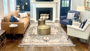 A living room with a fireplace, a television mounted above it, and a large rug.