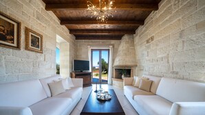 A living room with white sofas, a dark coffee table, stone walls, a wooden ceiling, a fireplace, and a TV.
