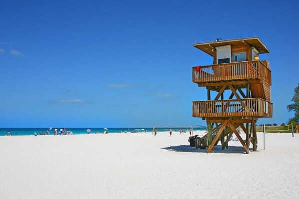 Una torre de salvavidas de madera en una playa bajo cielos azules y despejados.