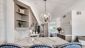 A modern kitchen with white cabinetry, a marble island, and wicker chairs.