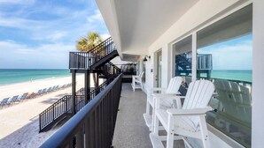 A balcony with white chairs, a view of the beach, and a staircase leading to the beach.