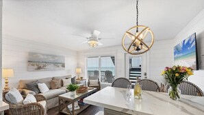A spacious living room with a large window, a ceiling fan, and a dining area with wicker furniture.