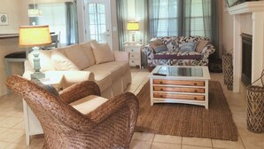 Un salon avec un canapé, une table basse, un fauteuil en osier, un téléviseur et une cheminée.
