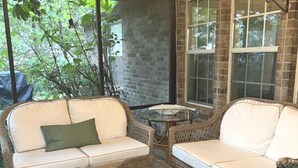 Un espace patio aménagé avec des meubles en osier, une table en verre décorée de coquillages et un mur en briques.