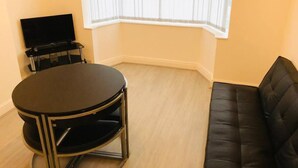 A corner room with a round table, a black sofa, and a TV on a stand. - 4 Bedroom Lovely home in Loughborough town & Uni (Loughborough)