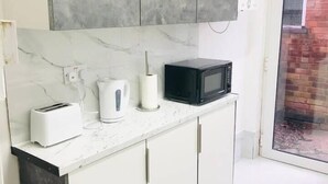 A modern kitchen with white cabinets, a marble countertop, a black microwave, a white kettle, and a toaster. - 4 Bedroom Lovely home in Loughborough town & Uni (Loughborough)