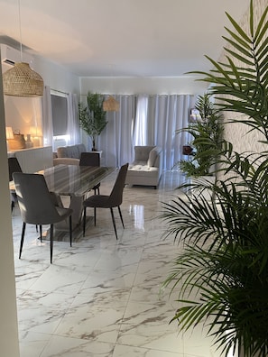 A modern living room with a marble floor, a dining table with chairs, a sofa, and a large potted plant.