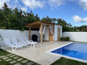 A poolside area with a pergola, lounge chairs, and a small covered seating area.