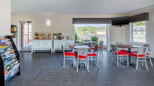 A dining area with a table and chairs, a television mounted on the wall, and a view of the outside. - Rodeway Inn Mystic (Mystic)
