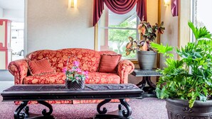 A red floral sofa with a striped pillow, a black table with a plant, and a large potted plant. - Rodeway Inn Mystic (Mystic)